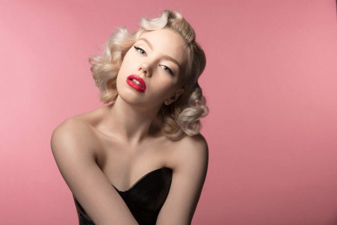 Blonde model with bright red lips posing in front of a pink backdrop